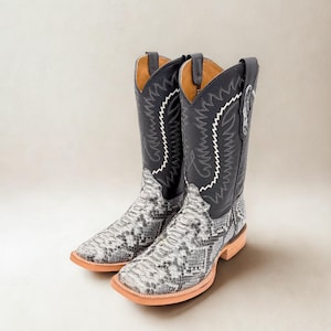 May include: A pair of cowboy boots with a black leather upper and a snakeskin pattern on the foot. The boots have white stitching and a square toe. The soles are a light brown color.