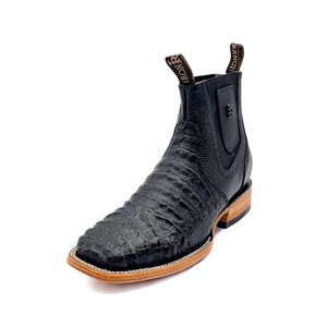 May include: Black leather ankle boot with a square toe and a textured, crocodile-like pattern. The boot has a pull tab with "RANCH IRON" printed on it. The sole is a light brown color with a white stitch.