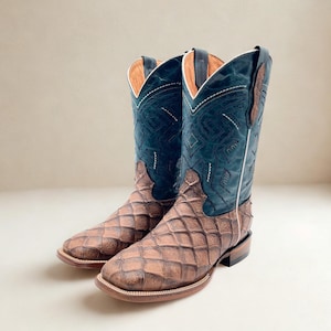 May include: A pair of cowboy boots with a brown, diamond-patterned foot and a dark blue leather upper. The boots have a white stitch design and a square toe. The interior is tan.