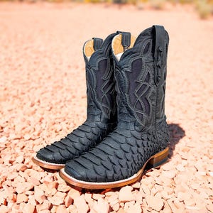 May include: A pair of black cowboy boots with a snakeskin pattern. The boots have a pointed toe and a decorative stitching pattern on the shaft.