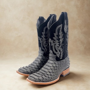 May include: A pair of cowboy boots with a gray, textured foot and a black suede shaft. The shaft features decorative stitching. The boots have a square toe and a light brown sole. The boots are approximately 12 inches tall.