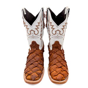 May include: A pair of cowboy boots with a white and brown design. The upper part of the boots is white with brown decorative stitching. The lower part of the boots is brown with a scale-like texture. The boots have a square toe.