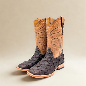 May include: A pair of cowboy boots with a unique design. The boots feature a dark brown, diamond-patterned vamp and a light brown, intricately designed shaft. The soles are light brown, and the boots have a square toe.