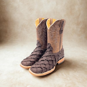 May include: A pair of brown cowboy boots with a unique scale-like texture on the foot and a classic stitched design on the shaft. The boots have a square toe and a light-colored sole, showcasing a blend of rustic and refined elements.