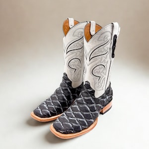 May include: A pair of cowboy boots with a black diamond-patterned vamp and white shaft. The shaft features intricate gray and black stitching. The boots have a square toe and a light brown sole. The uppers are white with decorative stitching.