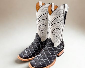May include: A pair of cowboy boots with a black diamond-patterned vamp and white shaft. The shaft features intricate gray and black stitching. The boots have a square toe and a light brown sole. The uppers are white with decorative stitching.