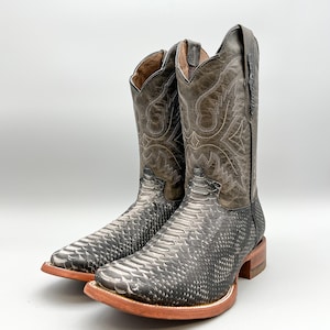 May include: A pair of black and grey cowboy boots with a snakeskin pattern. The boots have a pointed toe and a low heel.