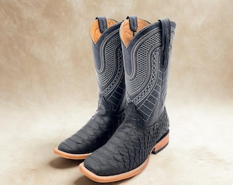 May include: A pair of black cowboy boots with a textured, scaly pattern on the foot and a smooth, stitched design on the upper shaft. The boots have a square toe and a light brown sole. The interior is a light tan color.