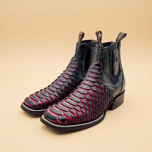 May include: A pair of black and red leather ankle boots. The boots feature a unique scale-like pattern in black with red accents. The soles are black with white stitching, and the heels are a dark brown color.