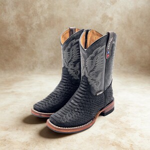 May include: A pair of black cowboy boots with a textured pattern on the foot and a decorative stitched design on the shaft. The boots have a brown sole and a pull tab at the top. The brand name "KEYWEST" is visible on the side.