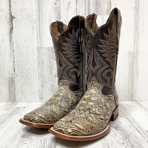 May include: A pair of brown leather cowboy boots with a decorative swirl pattern. The boots have a pointed toe and a brown leather heel.