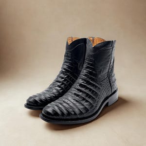 May include: A pair of black leather cowboy boots with a crocodile skin texture. The boots have a pointed toe, a low heel, and a pull-on design. The boots are displayed on a neutral background.