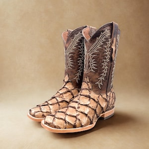 May include: A pair of brown cowboy boots with a unique design. The boots feature a textured, scale-like pattern on the lower portion and intricate stitching on the upper shaft. The boots have a square toe and a stacked heel.