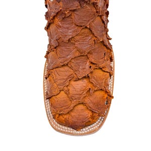May include: Close-up of a brown leather boot with a unique, textured design. The boot features a square toe and a white upper. The leather has a scale-like pattern, creating a distinctive look. The boot's construction is visible.