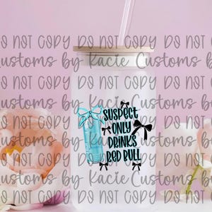 May include: A clear glass tumbler with a bamboo lid and a straw. The tumbler features a Red Bull can graphic and the text "Suspect Only Drinks Red Bull" with bow accents. The background is a soft pink.