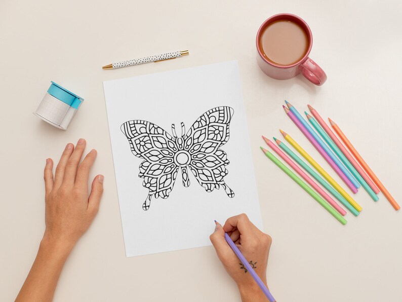 Peut inclure: Une page de coloriage de papillon noir et blanc avec des motifs complexes est en cours de coloriage avec un crayon de couleur violet. Une tasse de caf&eacute;, un stylo et un rouleau de ruban adh&eacute;sif sont sur la table. Un ensemble de crayons de couleur est &eacute;galement sur la table.
