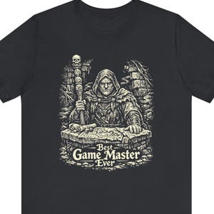May include: Black t-shirt featuring a detailed black and white illustration of a robed figure holding a staff, with the text "Best Game Master Ever." The graphic depicts a fantasy scene with a stone table and skull-topped staff.