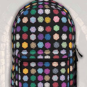 May include: A black backpack featuring an all-over repeating pattern of multi-colored twenty-sided dice. The bag includes a large main compartment, a smaller front zippered pocket, and a black mesh side pocket, all with black zippers and straps.
