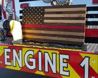 Op de afbeelding: Een Amerikaanse vlag van hout met een rode streep in het midden, gemonteerd op de achterkant van een rode brandweerwagen met de woorden "ENGINE 1" op de achterkant.