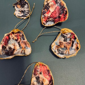 Puede incluir: Un conjunto de adornos navideños hechos con conchas de ostra. Cada concha presenta una escena invernal festiva, con borde dorado y una cuerda dorada para colgar. Las imágenes representan a Papá Noel y renos en un paisaje nevado.