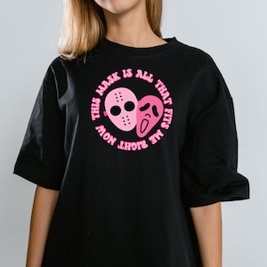 May include: Black t-shirt with a pink graphic of two horror movie masks and the text "This mask is all that fits me right now".