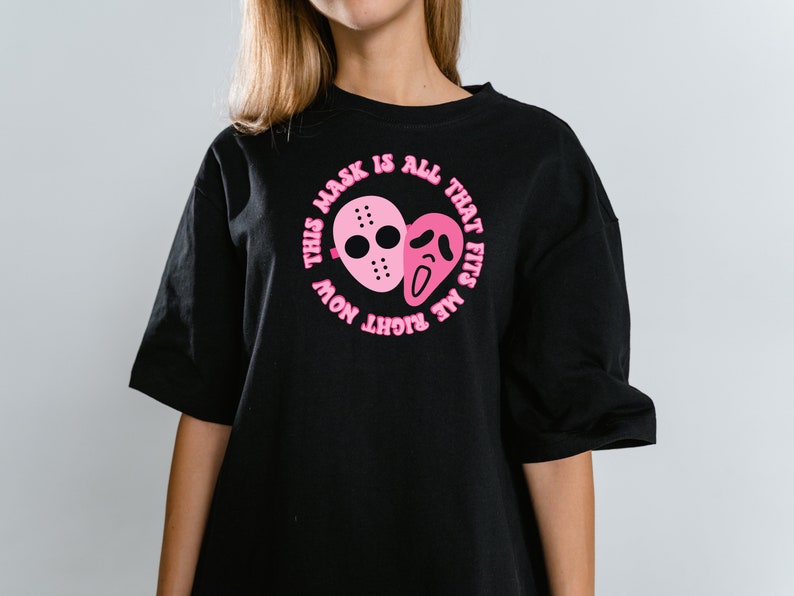 May include: Black t-shirt with a pink graphic of two horror movie masks and the text "This mask is all that fits me right now".