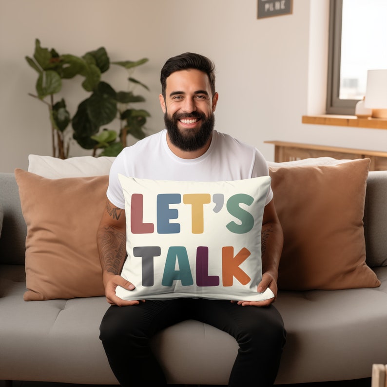 May include: A white throw pillow with the words "LET'S TALK" in colorful, bold letters. The pillow is being held by a person sitting on a couch.