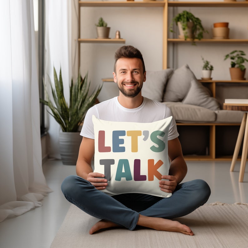 May include: A white throw pillow with the words "LET'S TALK" in colorful, stylized letters. The pillow is being held by a person sitting on the floor.