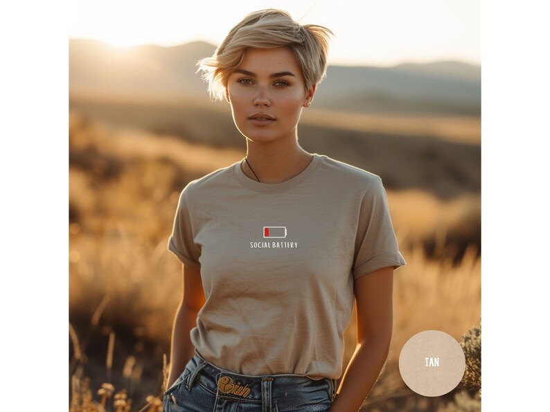 Op de afbeelding: Een beige T-shirt met een witte afbeelding van een bijna lege batterij en de tekst "Social Battery".