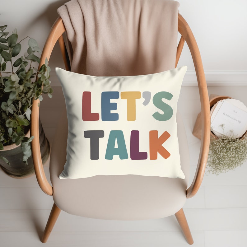 May include: A white throw pillow with the text "LET'S TALK" in colorful, bold letters. The letters are in shades of red, yellow, blue, green, gray, and purple.
