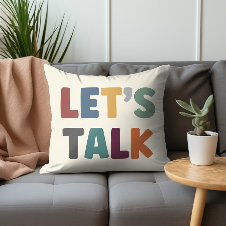 May include: A white throw pillow with the text "LET'S TALK" in colorful, stylized letters. The letters are in shades of red, blue, yellow, green, gray, purple, and orange.