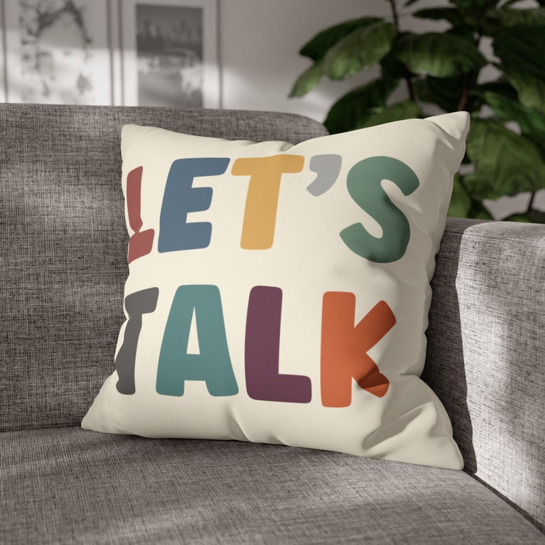 May include: A cream-colored throw pillow with the text "LET'S TALK" in colorful, bold letters. The letters are in shades of blue, yellow, green, purple, and orange.