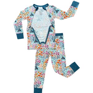 K&ouml;nnte beinhalten: Ein zweiteiliger Schlafanzug mit floralem Muster in Orange, Rosa, Blau und Gr&uuml;n auf wei&szlig;em Grund. Das lang&auml;rmlige Oberteil hat einen Rei&szlig;verschluss vorne und einen tealfarbenen Besatz. Die passende Hose hat tealfarbene B&uuml;ndchen.
