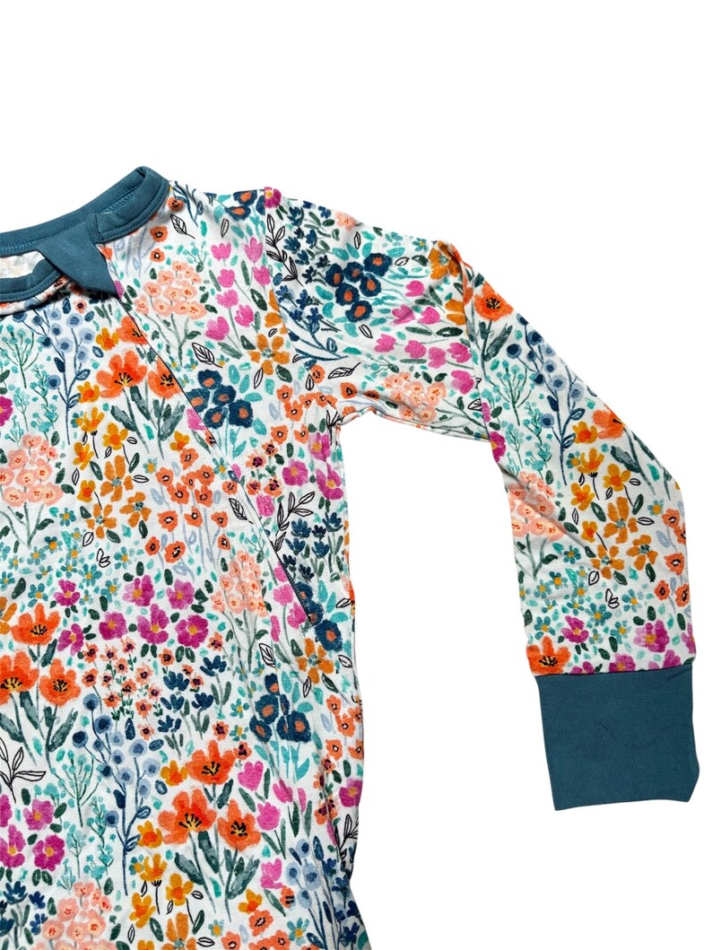 K&ouml;nnte beinhalten: Lang&auml;rmliges Kleidungsst&uuml;ck mit einem lebendigen Blumenmuster. Das Design zeigt einen wei&szlig;en Hintergrund, der mit orangefarbenen, rosa und blauen Blumen verziert ist. Die Manschetten und der Kragen sind einfarbig t&uuml;rkis. Das Kleidungsst&uuml;ck ist aus einem weichen, bequemen Material.