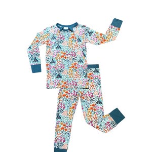 K&ouml;nnte beinhalten: Ein zweiteiliger Schlafanzug mit floralem Muster. Das lang&auml;rmlige Oberteil und die Hose haben einen wei&szlig;en Hintergrund mit bunten Blumen in Rosa, Orange und Blau. Die B&uuml;ndchen und der Halsausschnitt sind teal.