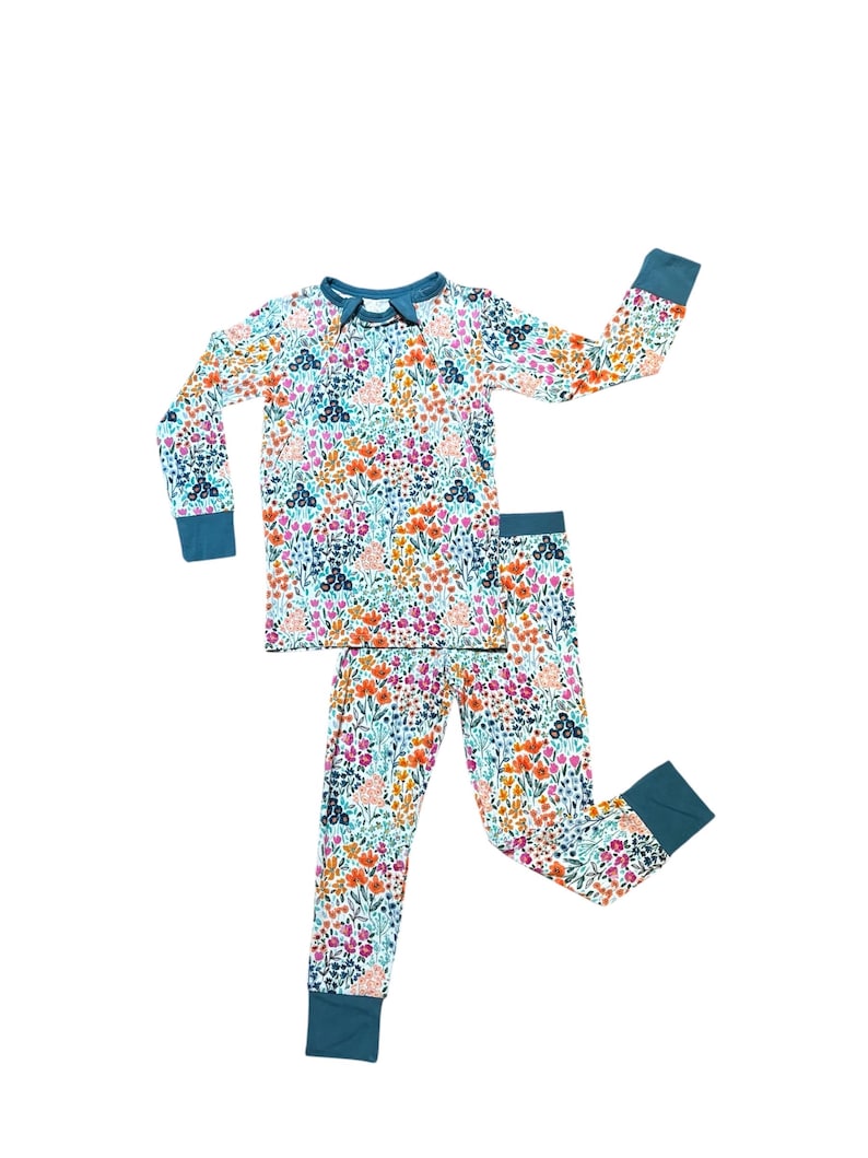 K&ouml;nnte beinhalten: Ein zweiteiliger Schlafanzug mit floralem Muster. Das lang&auml;rmlige Oberteil und die Hose haben einen wei&szlig;en Hintergrund mit bunten Blumen in Rosa, Orange und Blau. Die B&uuml;ndchen und der Halsausschnitt sind teal.