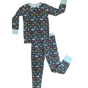 Puede incluir: Un conjunto de pijama de dos piezas con un estampado de tractores coloridos sobre un fondo verde azulado oscuro. La parte superior de manga larga y los pantalones tienen pu&ntilde;os y ribetes de color azul claro. El pijama est&aacute; dise&ntilde;ado para la comodidad y el sue&ntilde;o.