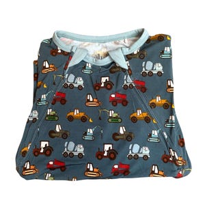 Puede incluir: Un pijama azul para beb&eacute; con un estampado de veh&iacute;culos de construcci&oacute;n coloridos, incluyendo tractores, hormigoneras y excavadoras. El pijama tiene un ribete azul claro alrededor del cuello y las mangas.