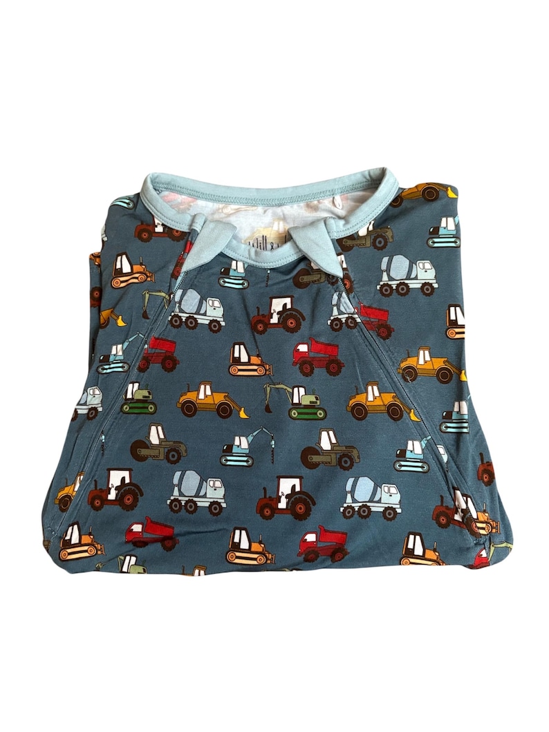 Puede incluir: Un pijama azul para beb&eacute; con un estampado de veh&iacute;culos de construcci&oacute;n coloridos, incluyendo tractores, hormigoneras y excavadoras. El pijama tiene un ribete azul claro alrededor del cuello y las mangas.