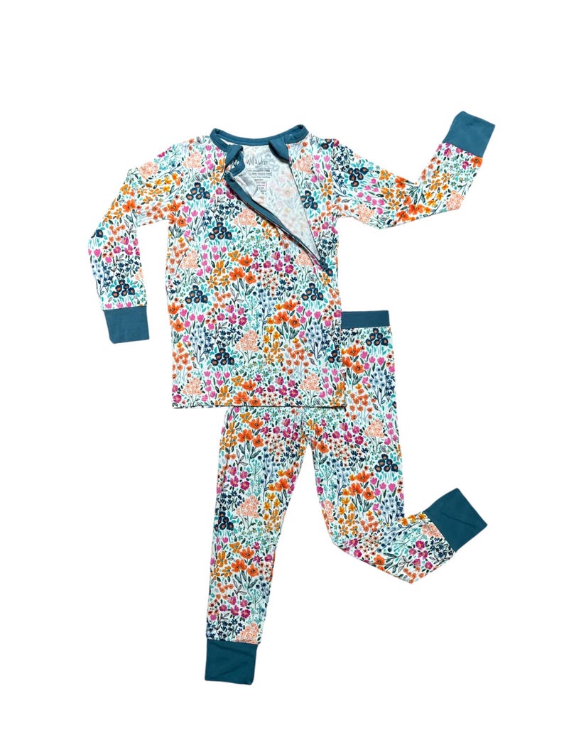 K&ouml;nnte beinhalten: Pyjama-Set mit floralem Muster und tealfarbenem Rei&szlig;verschluss, B&uuml;ndchen und Ausschnitt. Das lang&auml;rmlige Oberteil und die Hose zeigen ein farbenfrohes Blumenmuster in Rosa, Orange und Blau auf hellem Hintergrund.