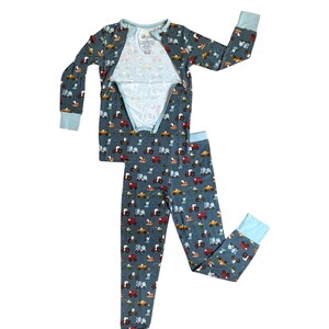 Puede incluir: Un conjunto de pijama de dos piezas en un color azul gris&aacute;ceo apagado, estampado con tractores coloridos. La parte superior de manga larga y los pantalones tienen pu&ntilde;os y ribetes de color azul claro. La parte superior tiene una abertura parcial.