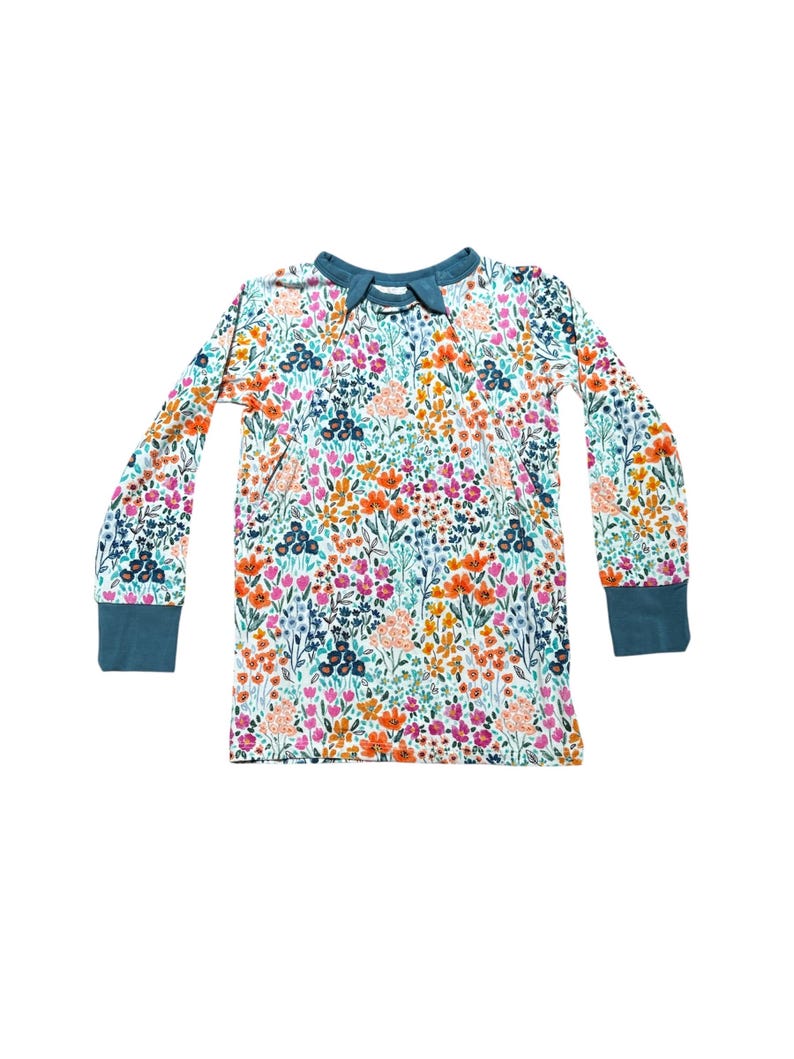 K&ouml;nnte beinhalten: Ein lang&auml;rmliges Shirt mit floralem Muster. Das Shirt hat einen wei&szlig;en Hintergrund mit einem farbenfrohen Blumendesign in Orange-, Rosa-, Blau- und Gr&uuml;nt&ouml;nen. Der Kragen und die Manschetten sind einfarbig t&uuml;rkis. Das Shirt ist aus einem weichen, bequemen Material.