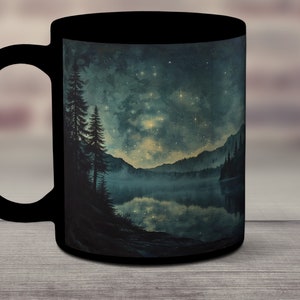 May include: Black ceramic mug with a scenic image of a lake surrounded by trees and mountains under a starry night sky.