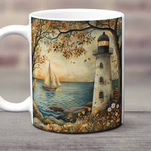May include: White ceramic mug with a colorful illustration of a lighthouse on a rocky shore with a sailboat in the water. The scene is framed by trees with autumn leaves.