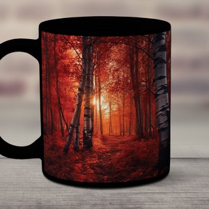 May include: A black ceramic mug with a colorful image of a forest path in autumn. The path is lined with trees with red leaves and the sun is shining through the branches.