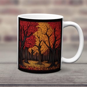 K&ouml;nnte beinhalten: Wei&szlig;e Keramiktasse mit schwarzem Rand und einer farbenfrohen Illustration einer Waldszene. Die B&auml;ume sind stilisiert und haben rote, orange und gelbe Bl&auml;tter. Der Boden ist mit heruntergefallenen Bl&auml;ttern bedeckt.