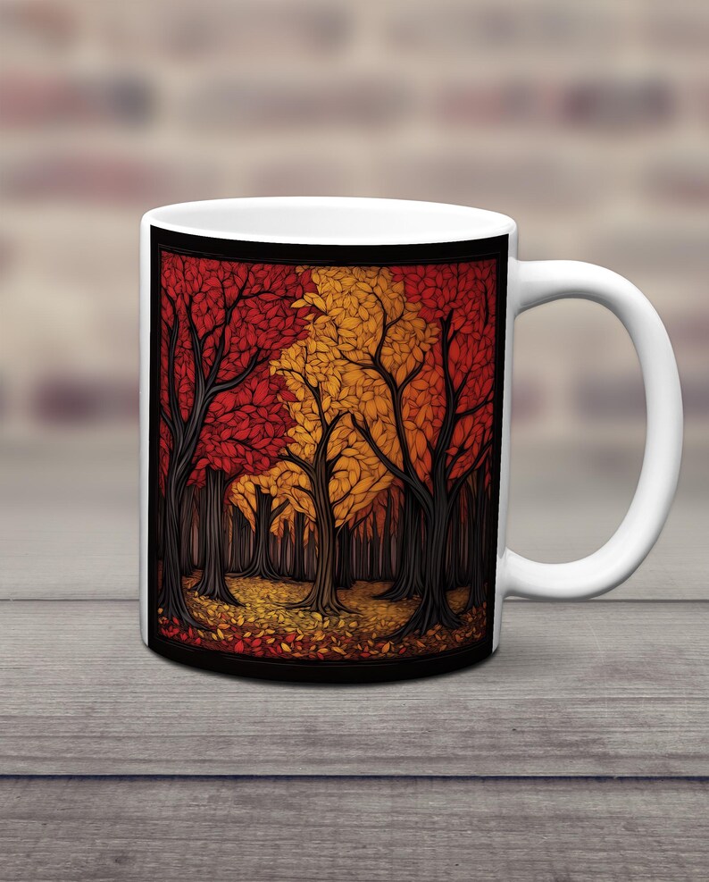 K&ouml;nnte beinhalten: Wei&szlig;e Keramiktasse mit schwarzem Rand und einer farbenfrohen Illustration einer Waldszene. Die B&auml;ume sind stilisiert und haben rote, orange und gelbe Bl&auml;tter. Der Boden ist mit heruntergefallenen Bl&auml;ttern bedeckt.