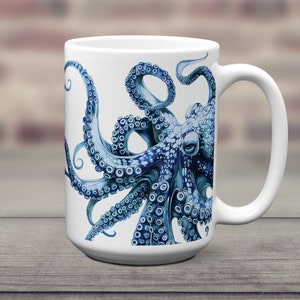 May include: A white ceramic mug featuring a detailed illustration of a blue octopus with prominent suckers on its tentacles. The octopus design wraps around the front of the mug, showcasing intricate textures and shades of deep and light blue.