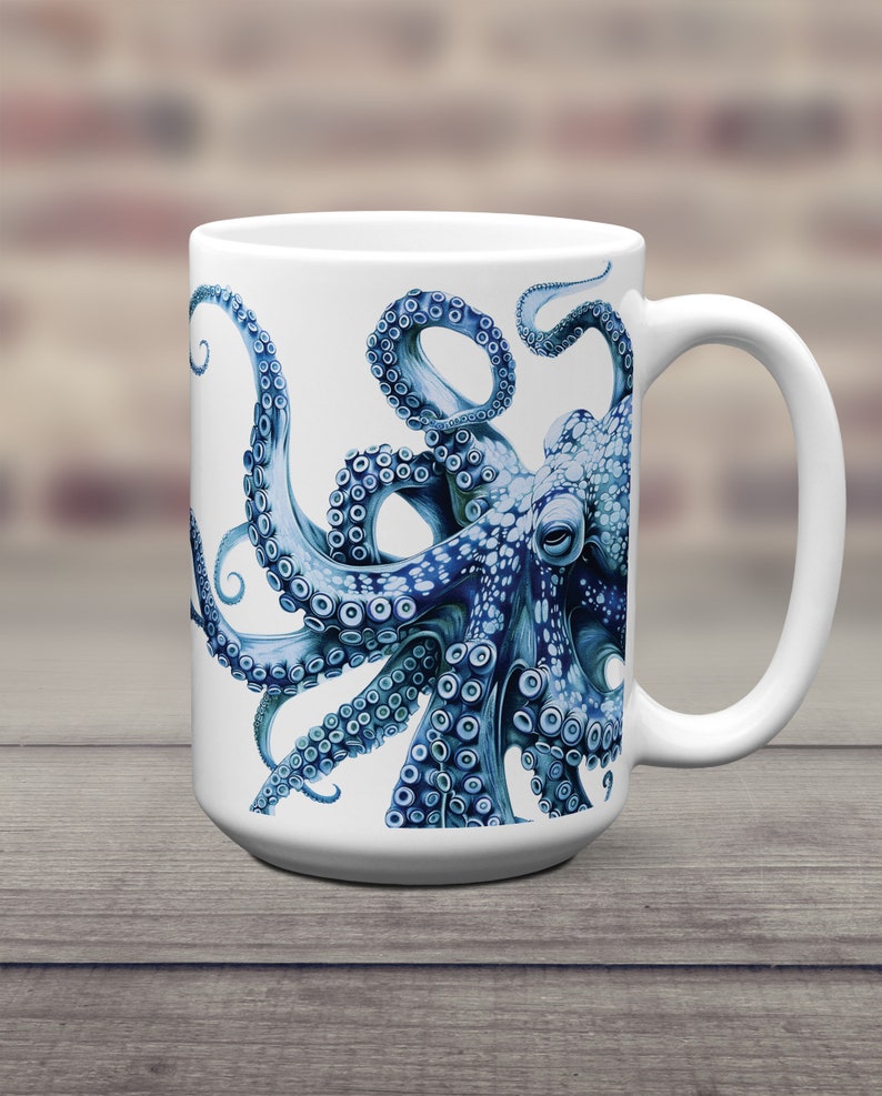 May include: A white ceramic mug featuring a detailed illustration of a blue octopus with prominent suckers on its tentacles. The octopus design wraps around the front of the mug, showcasing intricate textures and shades of deep and light blue.