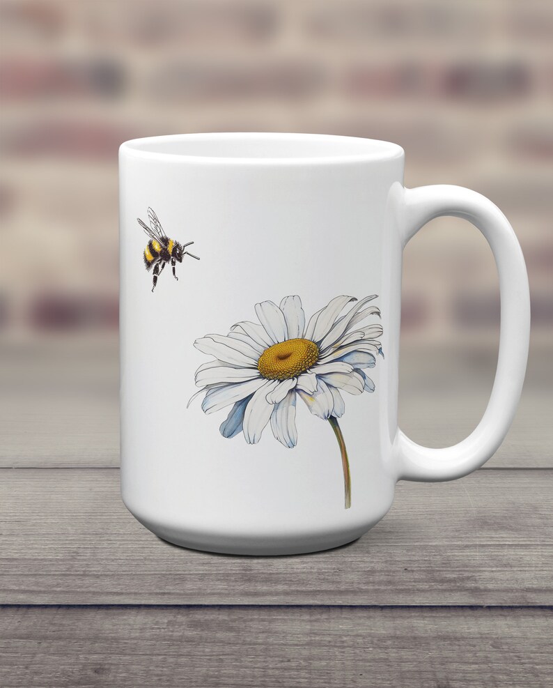 May include: White ceramic mug with a graphic of a bumblebee flying towards a white daisy with a yellow center.